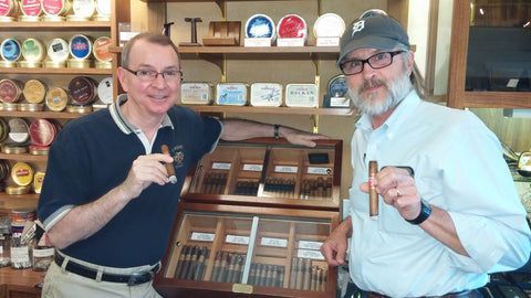 Two men are standing next to each other holding cigars in a store.