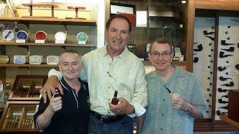 Three men are posing for a picture while one of them is holding a pipe.