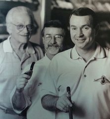 A black and white photo of three men standing next to each other holding cigars.