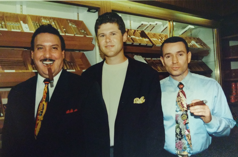 Three men are posing for a picture in front of a display of cigars