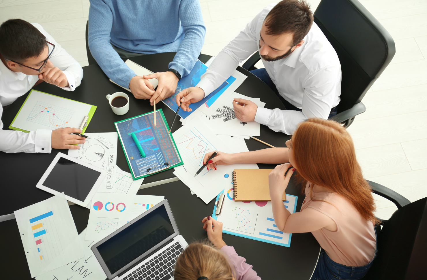 A group of people are sitting around a table with papers and laptops.