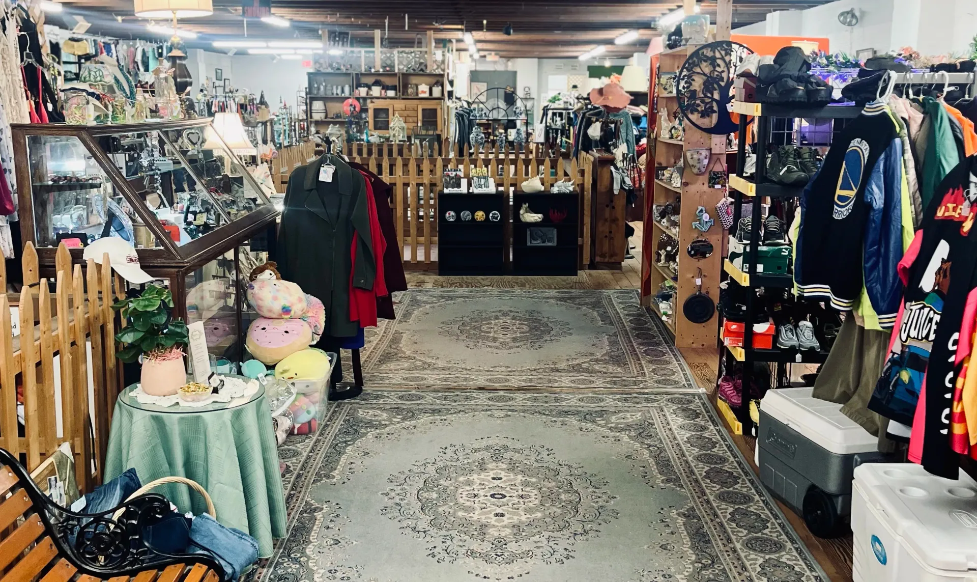 The interior of a vintage shop featuring clothing racks, display cases, and a patterned rug leading to the back area.