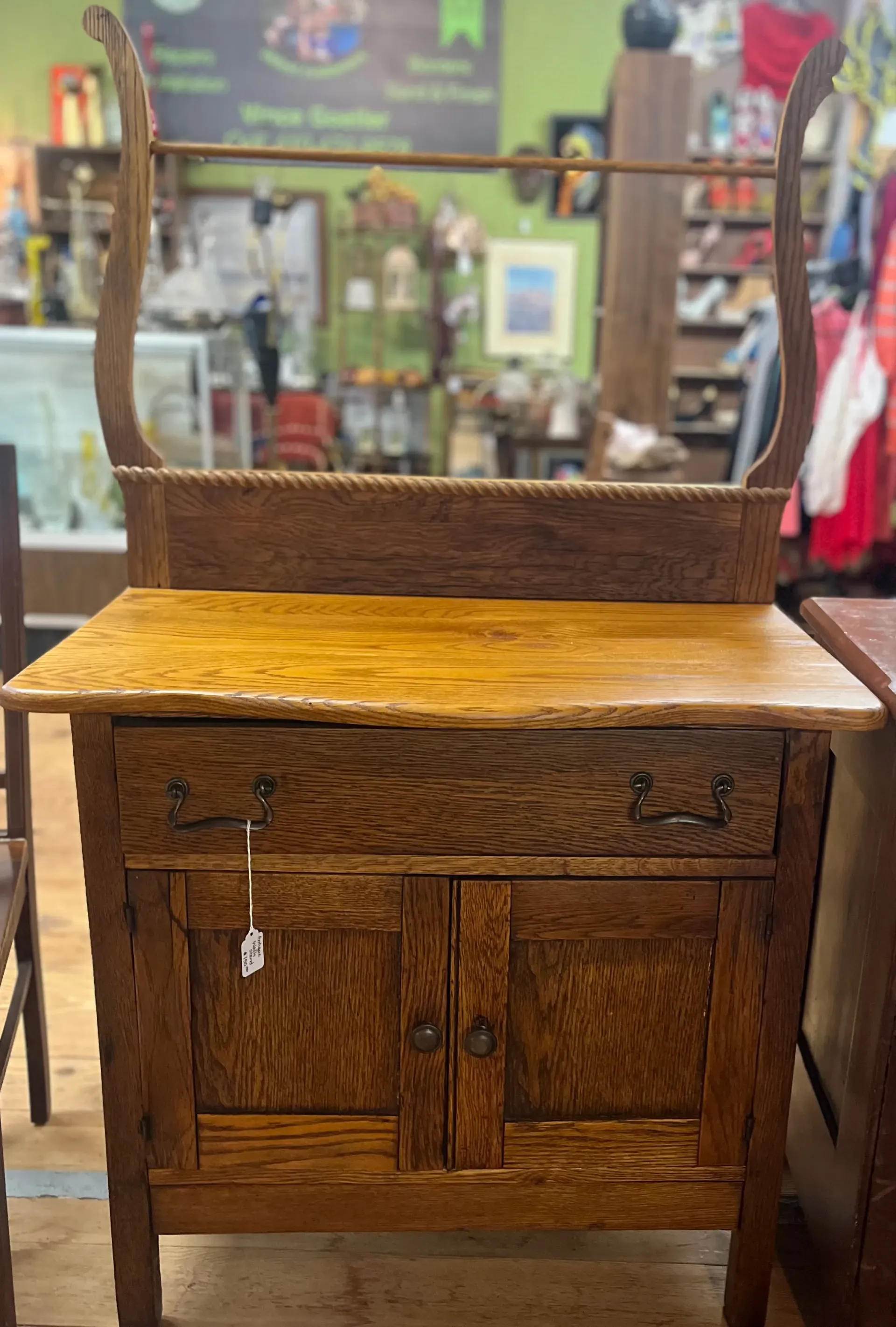 Antique oak washstand with a towel bar, carved uprights, a drawer, and two cabinet doors in a retail shop.