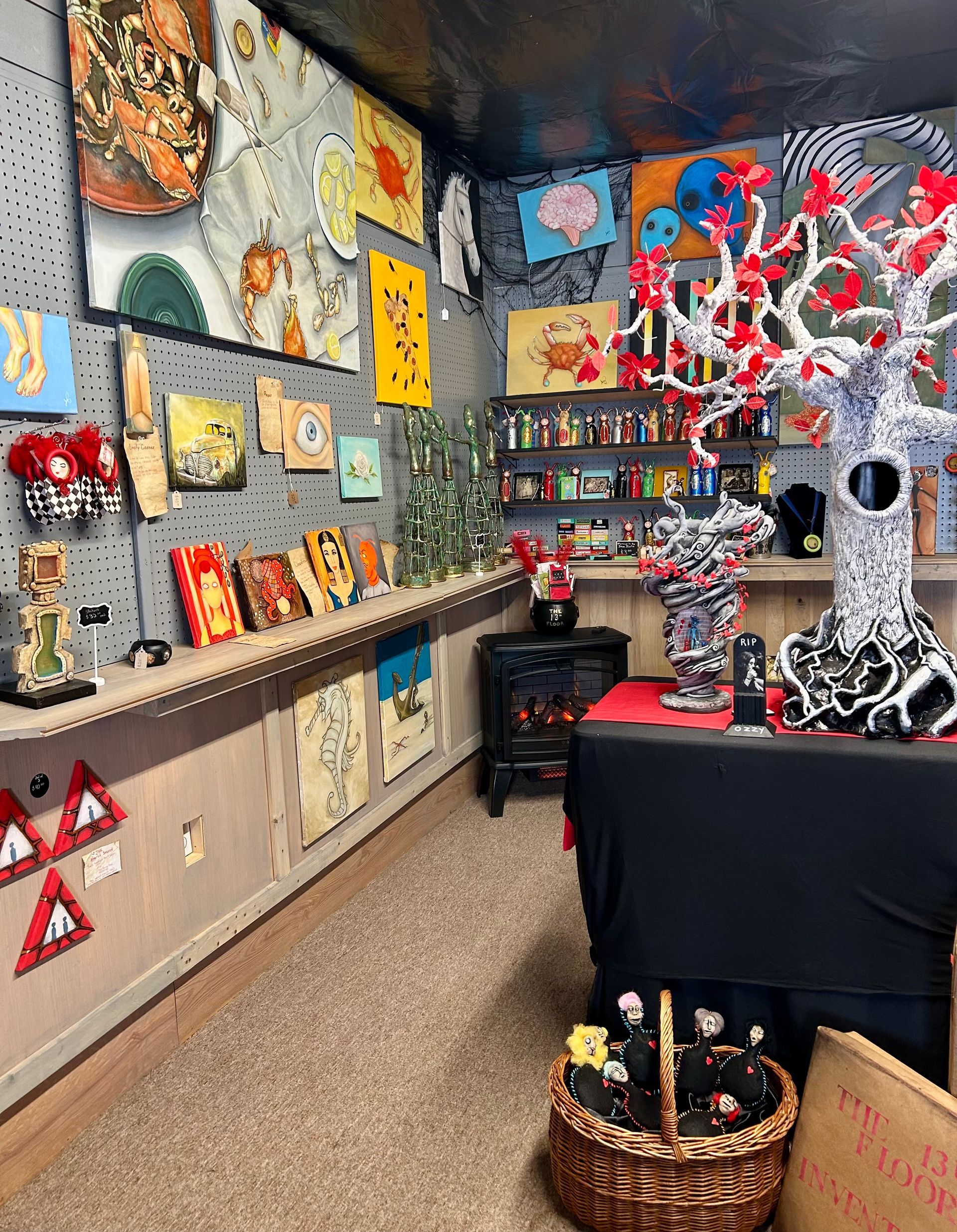 A crime scene display featuring a chalk outline on the floor, red-leafed decorative tree, and boxes in a studio gallery.