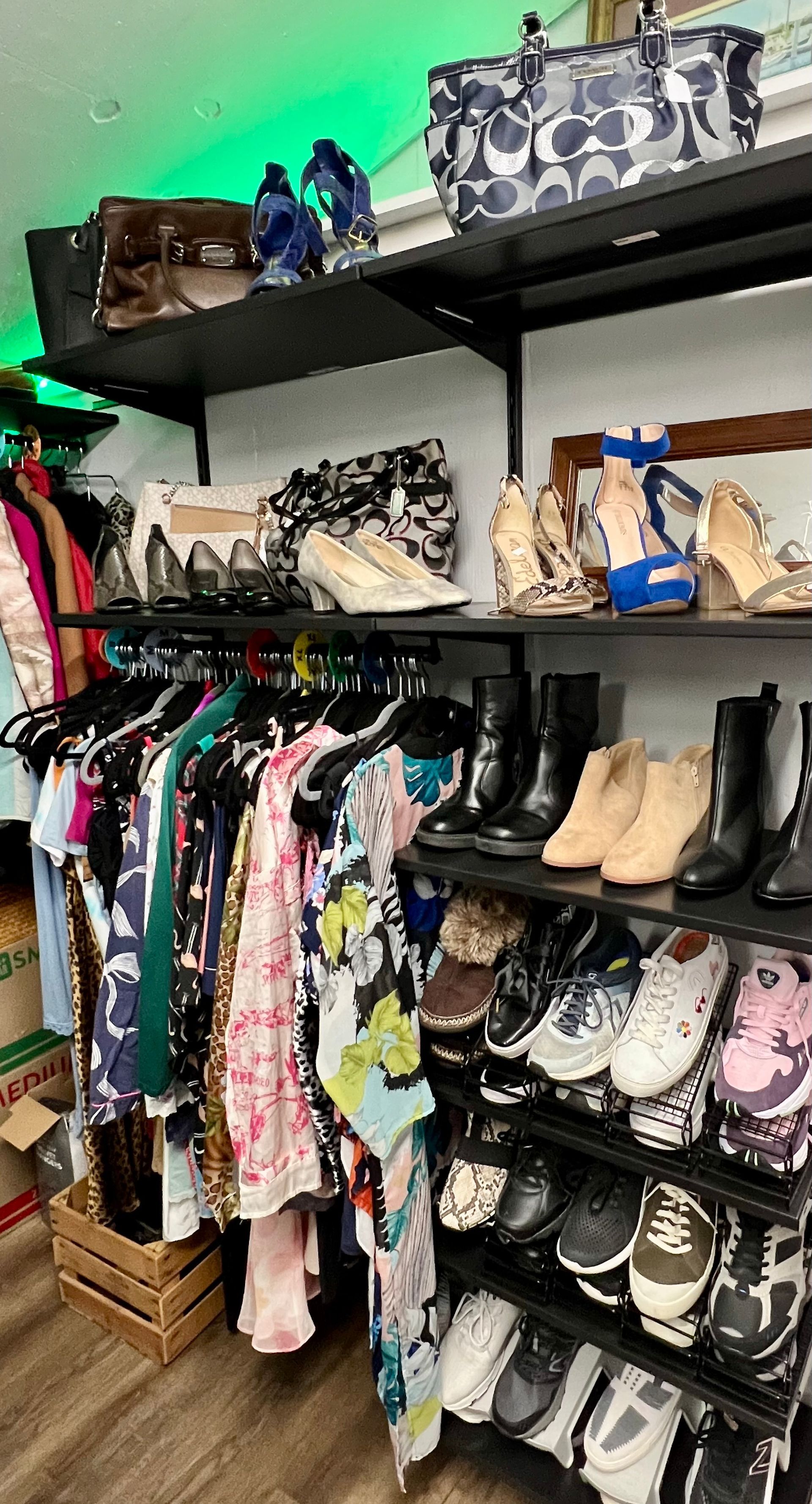 Clothing and shoes displayed on shelves and hanging racks in a retail store.