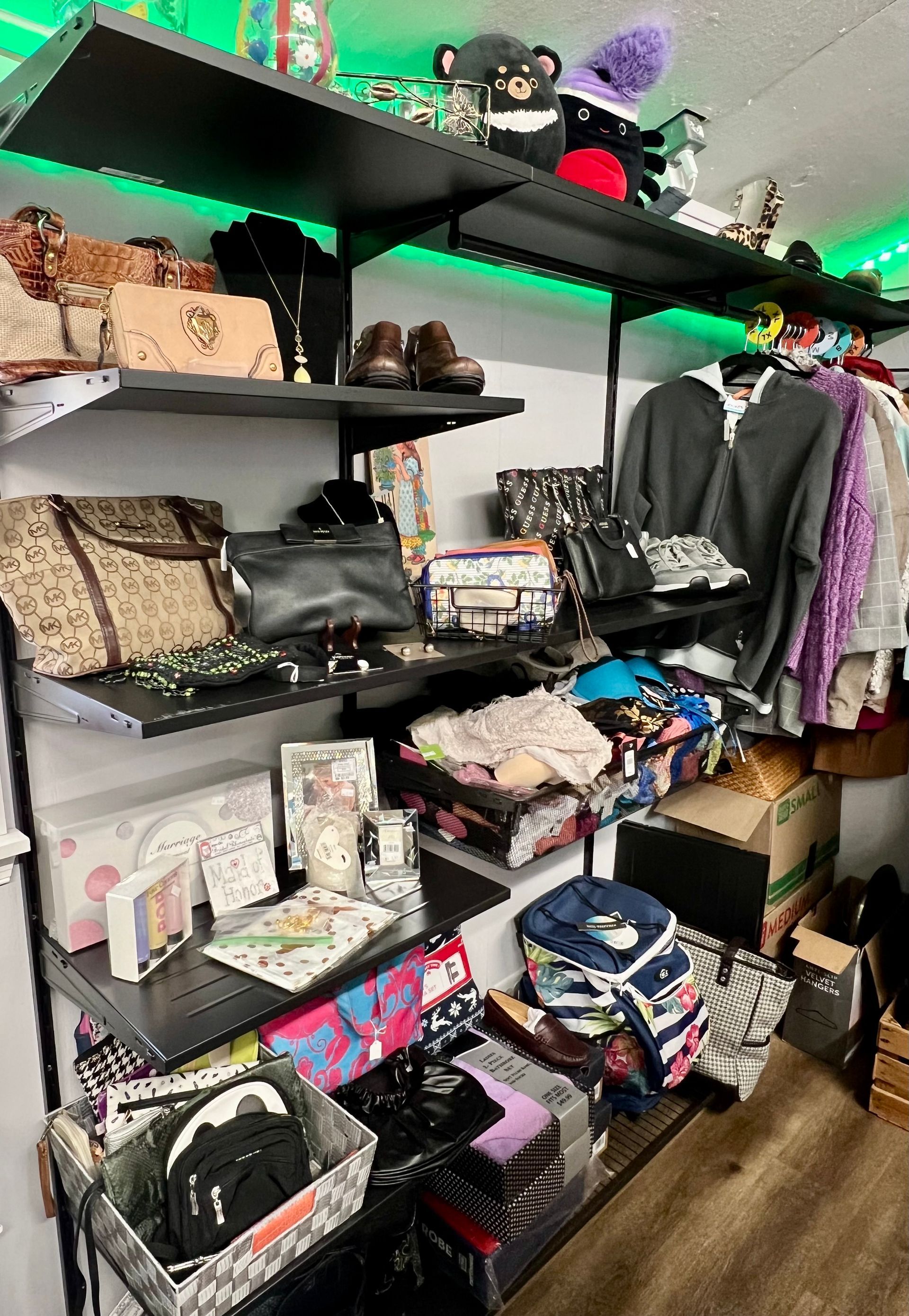 Shelving units filled with handbags, clothing, personal items, and plush toys in a room illuminated by green LED lights.