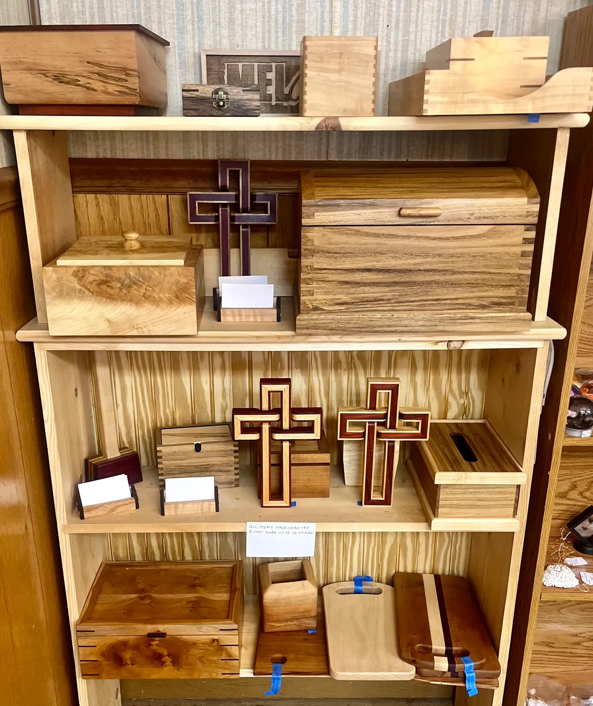 Handcrafted wooden boxes and decorative crosses displayed on tiered wooden shelving.