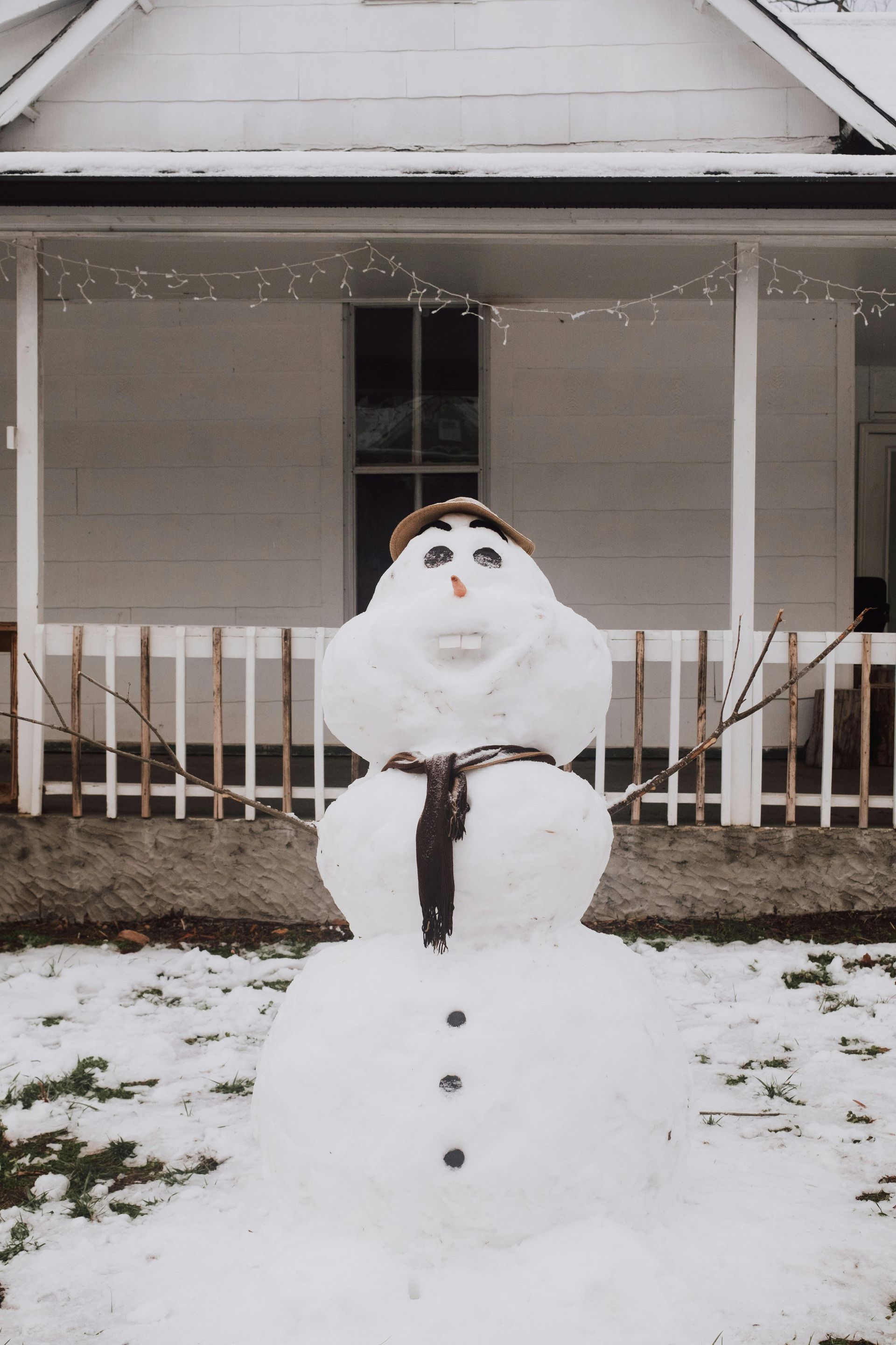 A snowman is standing in front of a white house