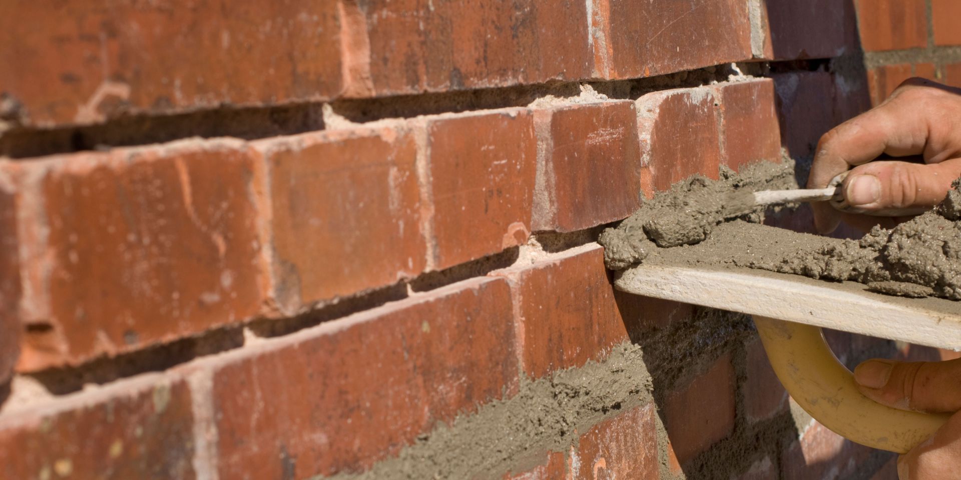 A hand using a trowel to apply mortar to the joints of a brick wall.