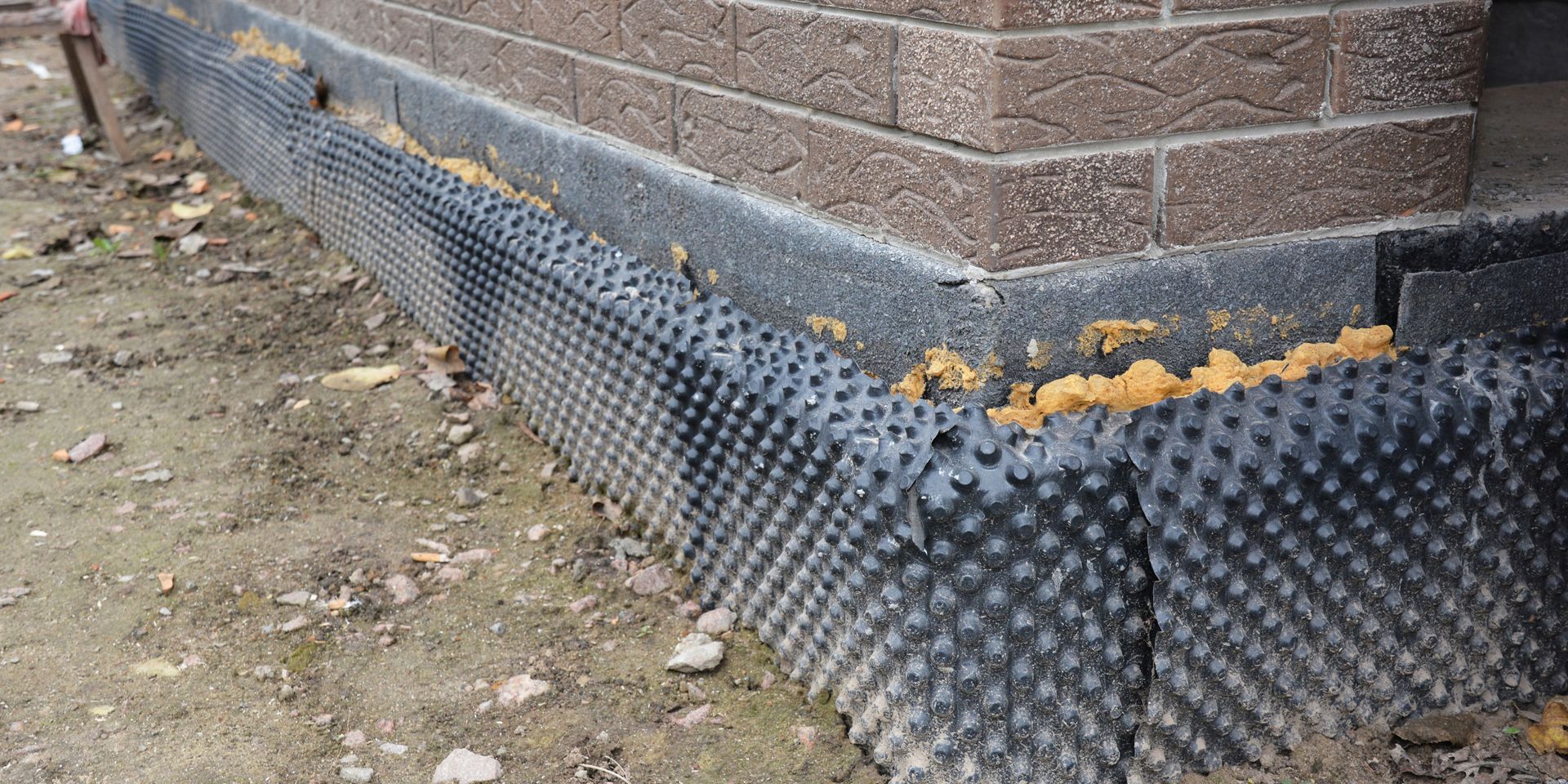 Black dimpled drainage membrane installed on the foundation of a brick building.