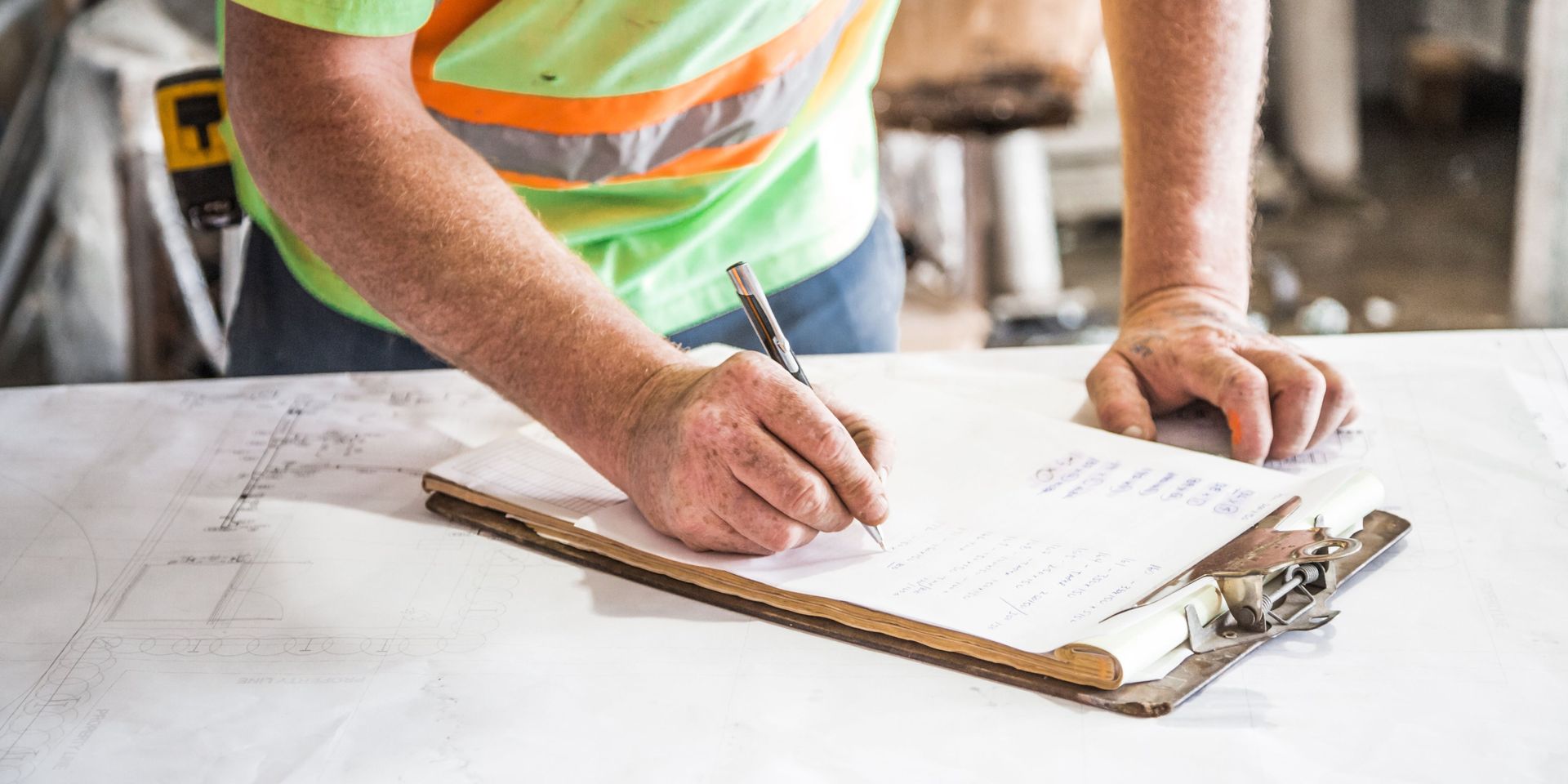 A construction worker is writing on a clipboard with a pen.