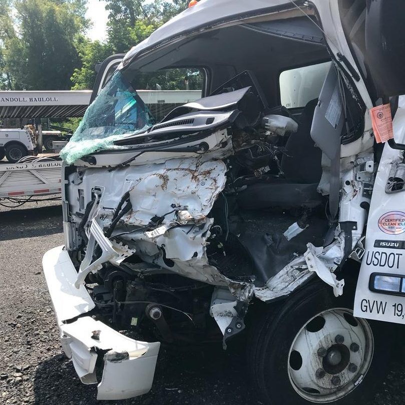 Damaged white truck after a collision, with a crushed front and shattered windshield.