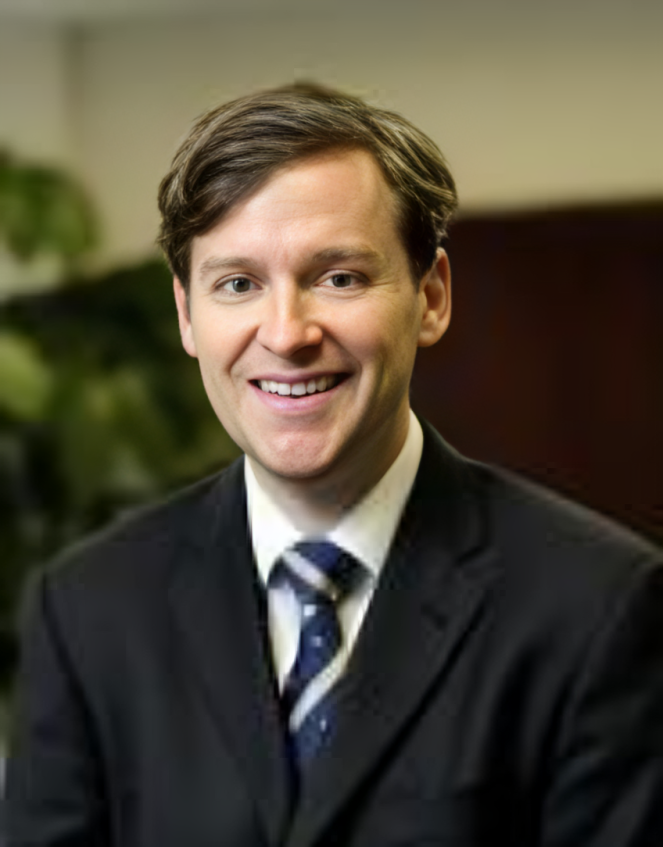 Man in a suit smiles at the camera, inside office, looking friendly.