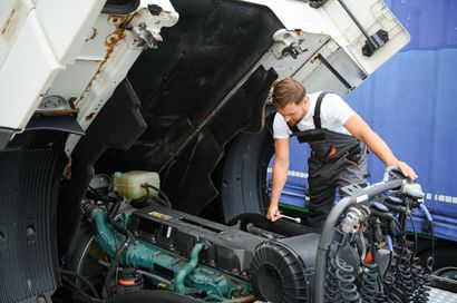 Mechanic inspecting a truck engine with the hood open, outdoors.