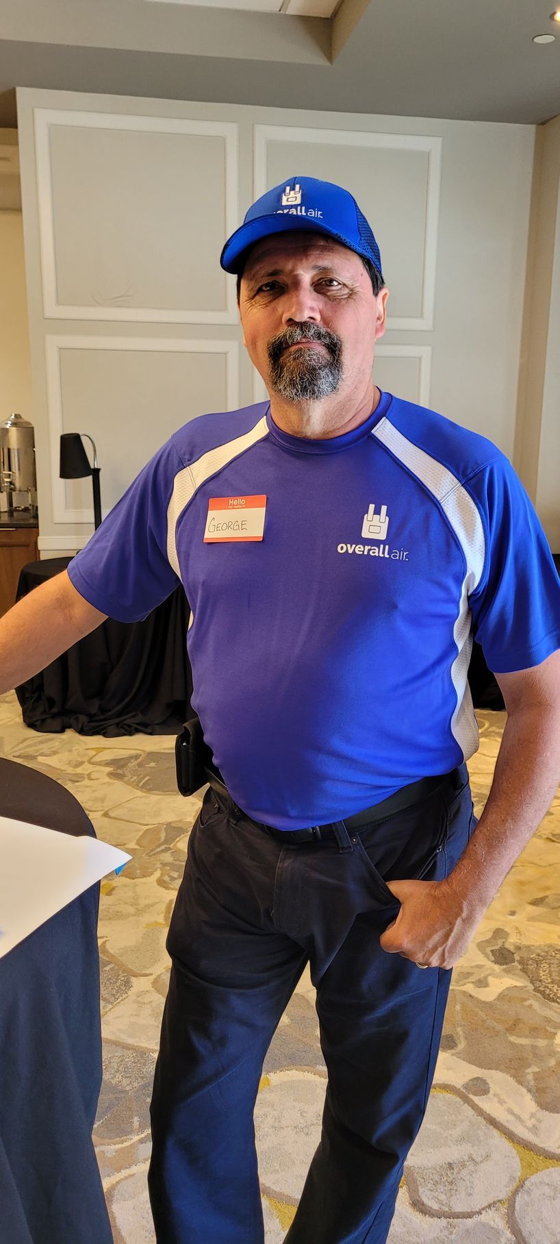 A person wearing a blue shirt with white accents and a blue cap standing in a room, looking toward the camera.