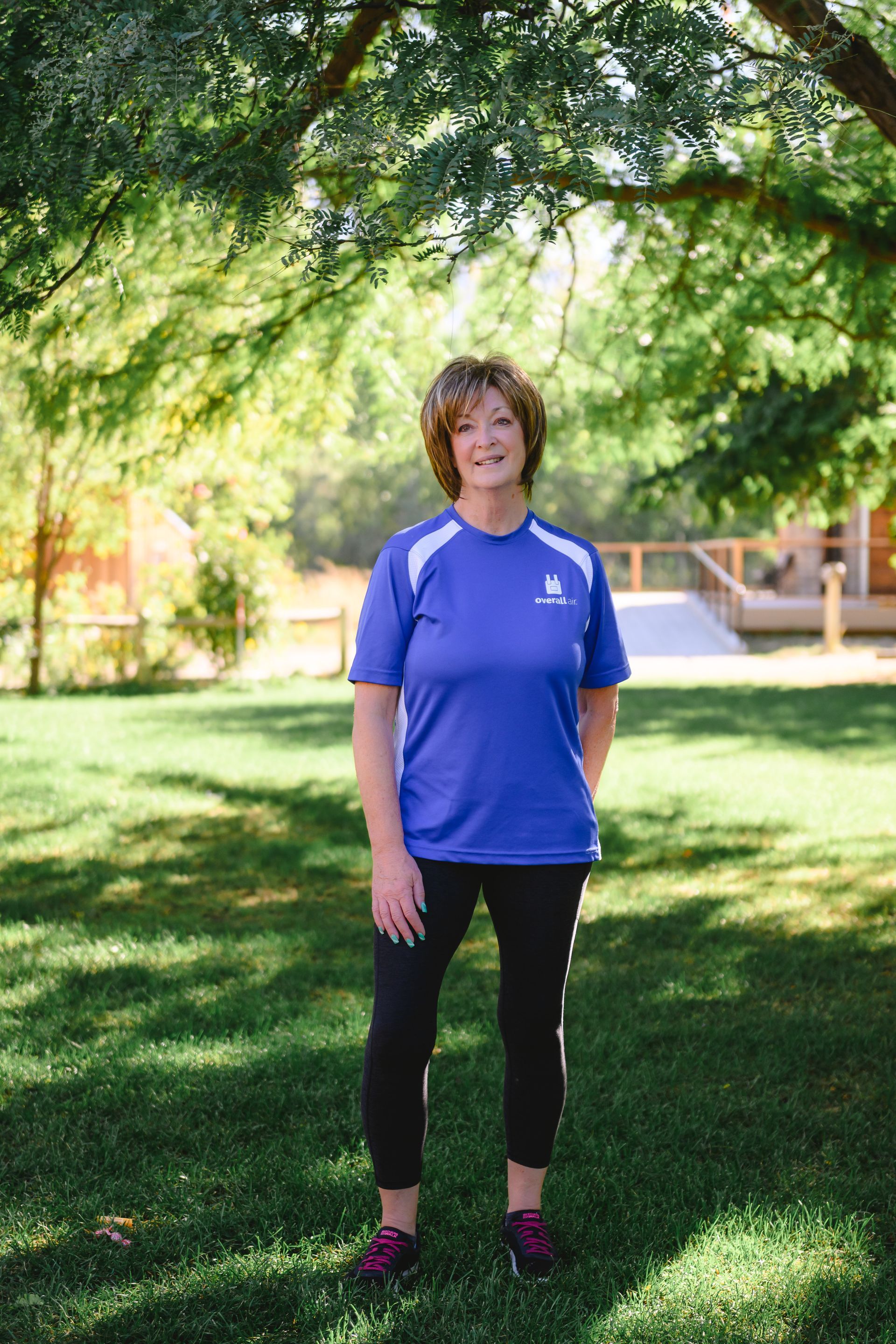 A person in a blue athletic shirt and black pants standing on a green lawn beneath a tree.