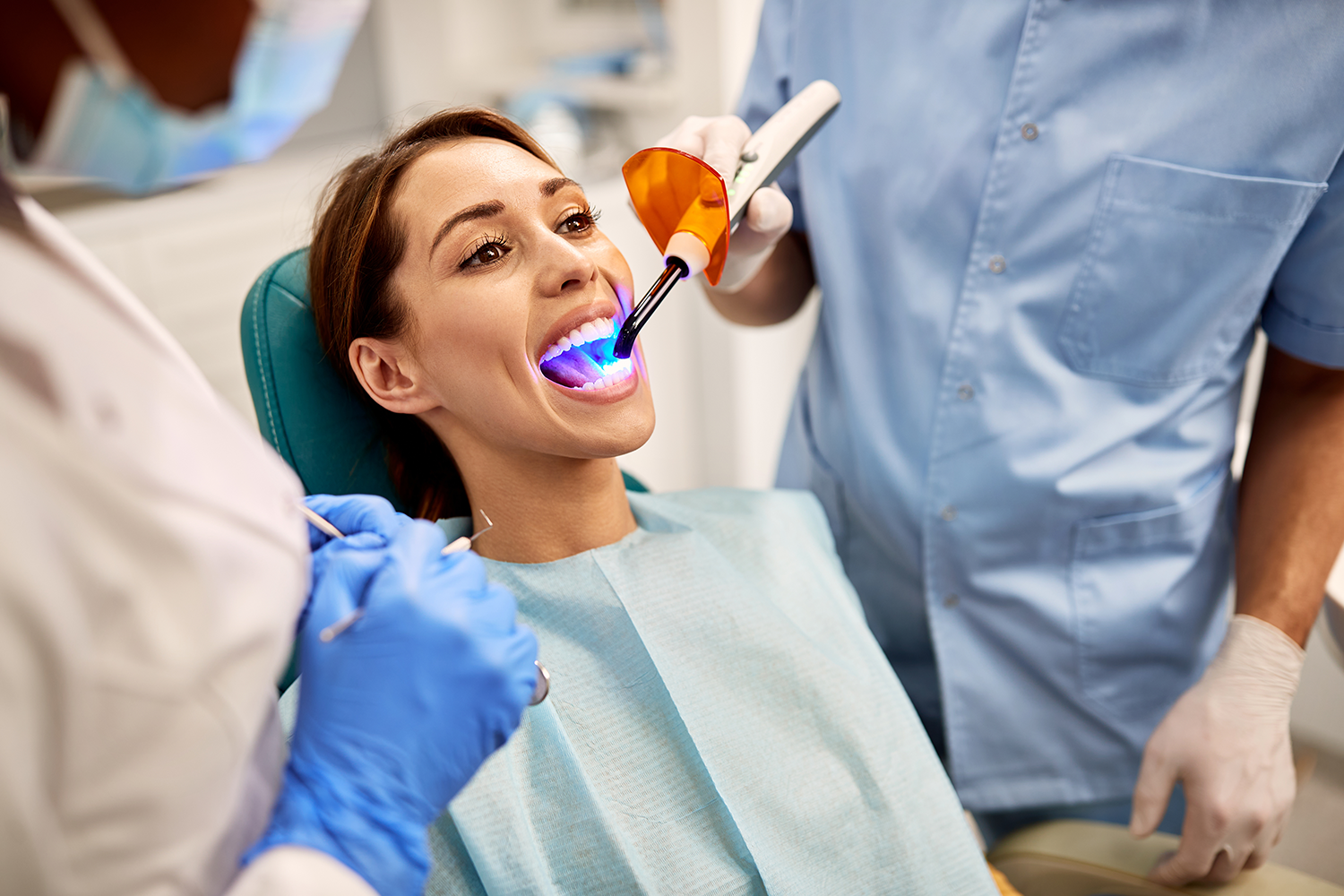 a woman is sitting in a dental chair getting her teeth whitened by a dentist.
