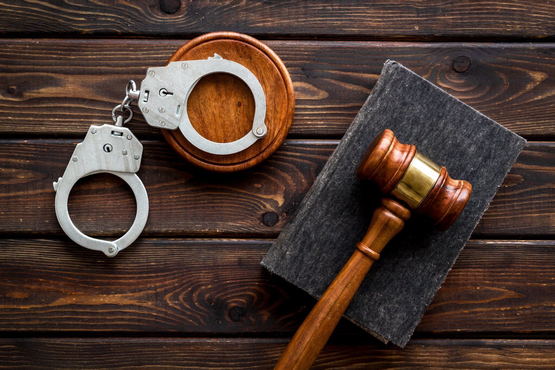 A pair of handcuffs and a judge 's gavel on a wooden table.