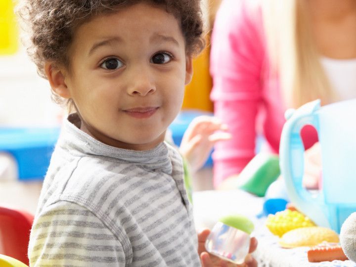 A young boy is sitting at a table with toys and looking at the camera.