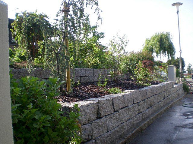Eine Steinmauer umgibt einen Garten mit Bäumen und Sträuchern