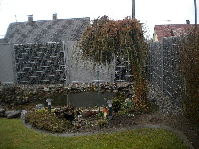 Ein Garten mit einem Teich und einem Zaun darum herum.