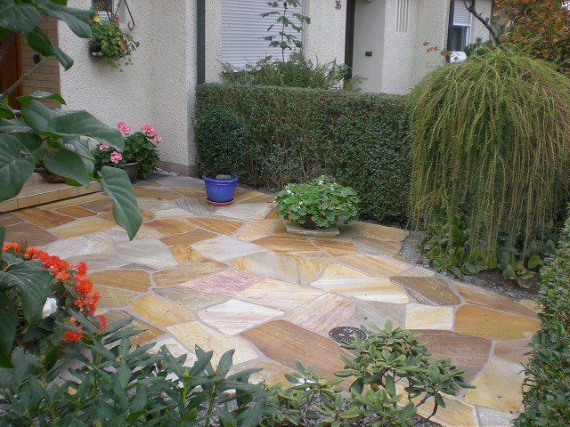 Ein Steinweg vor einem Haus mit Topfpflanzen und Blumen.