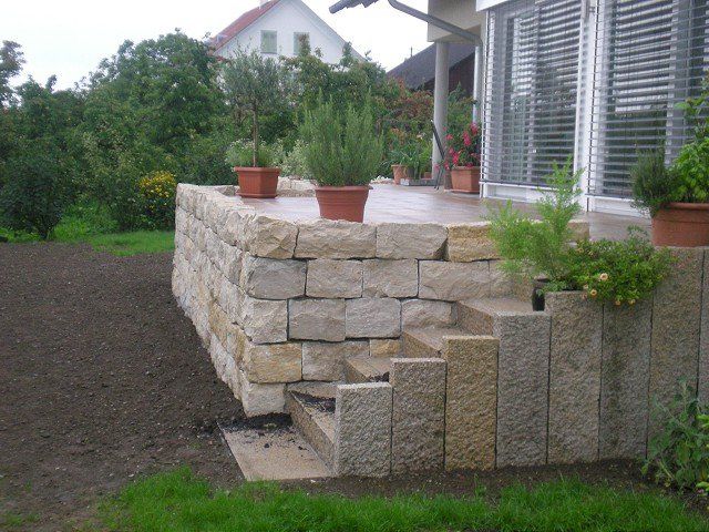 Eine Steinmauer mit Treppen und Topfpflanzen vor einem Haus