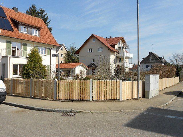 Ein weißer Lieferwagen steht am Straßenrand neben einem Holzzaun