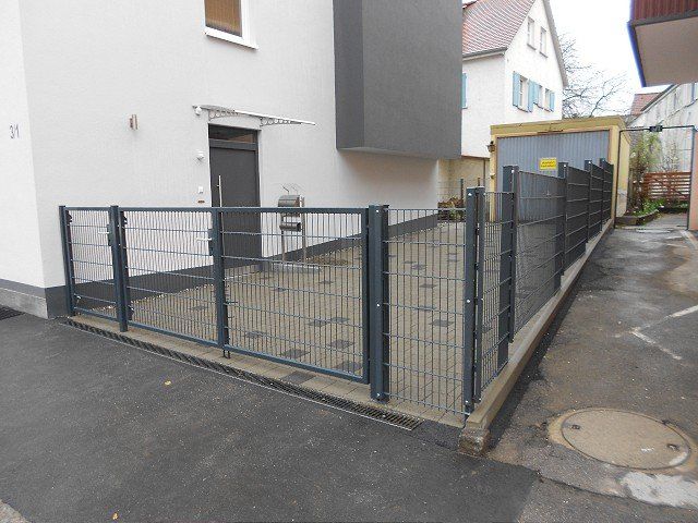 Ein Zaun umgibt eine Einfahrt vor einem weißen Gebäude