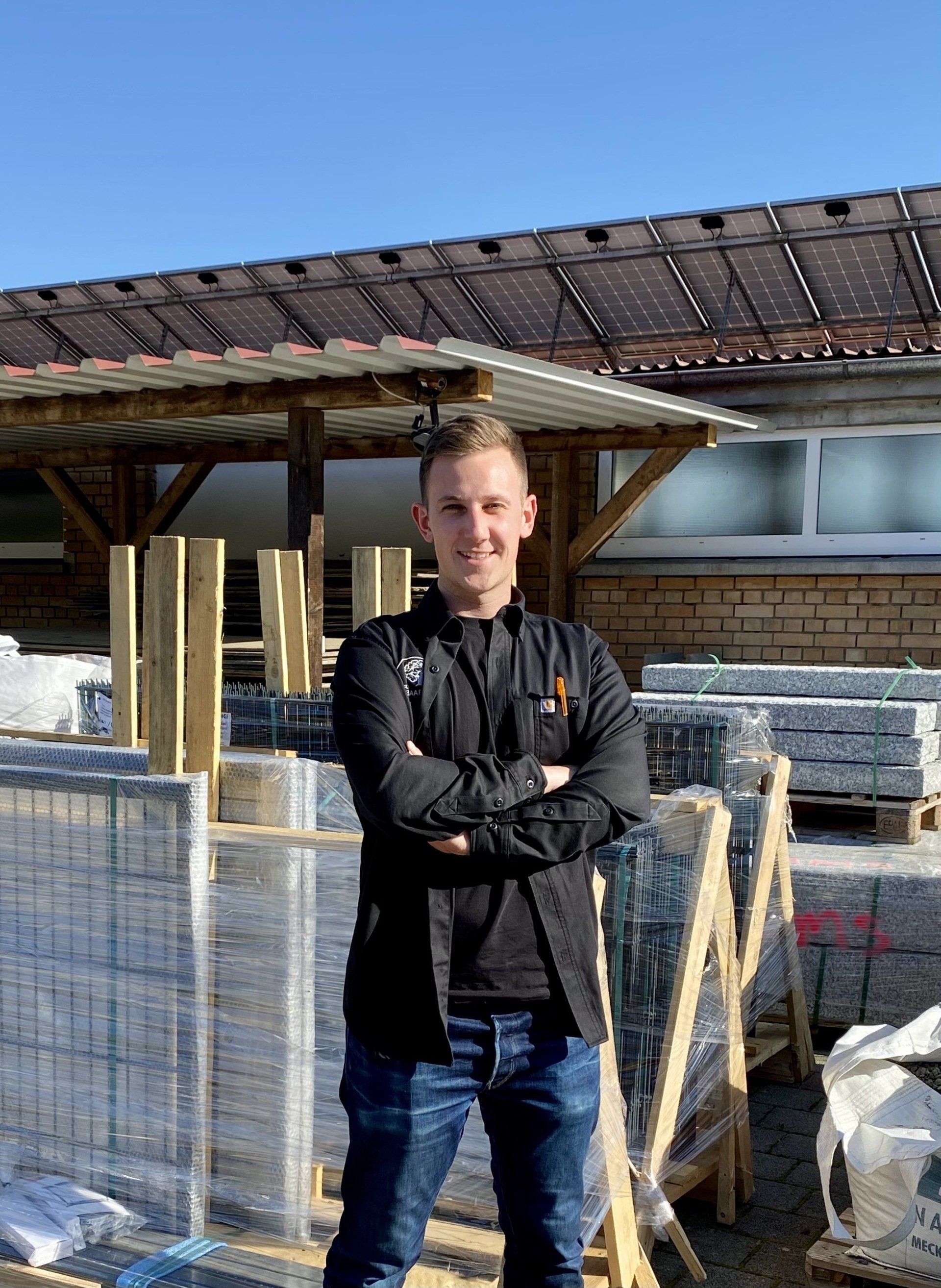 Ein Mann steht mit verschränkten Armen vor einem Gebäude.