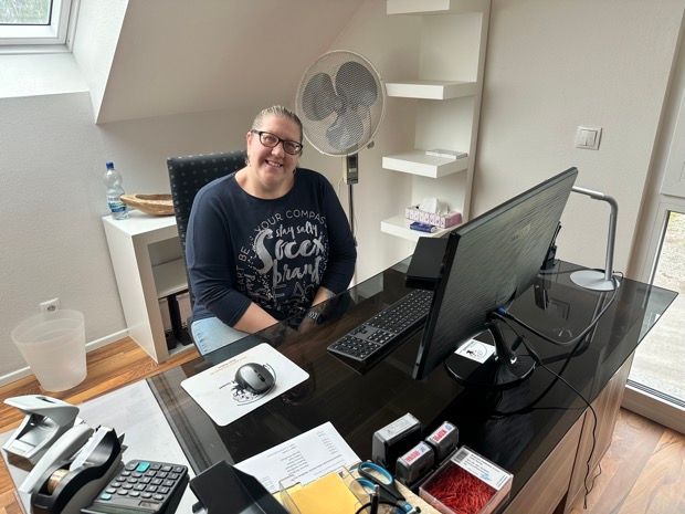 Eine Frau sitzt an einem Schreibtisch mit einem Computer und einem Ventilator.