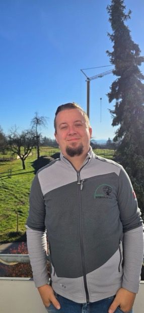 Ein Mann steht mit verschränkten Armen vor einem Gebäude.