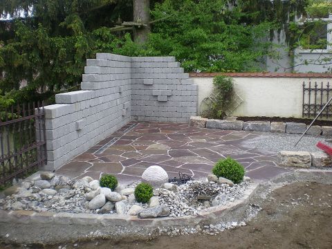 Eine Ziegelmauer ist von Felsen und Pflanzen umgeben