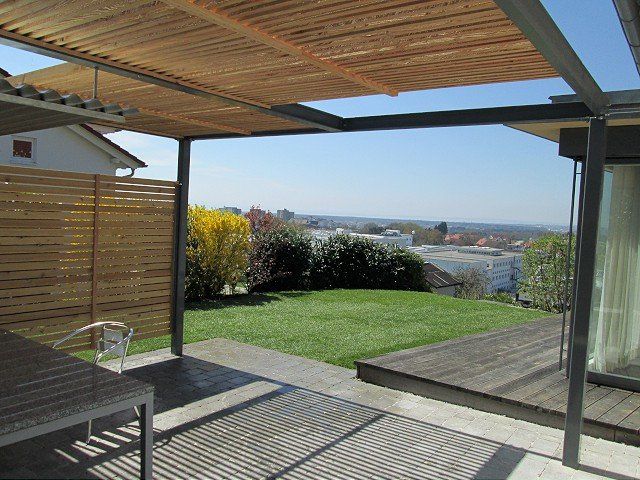 Eine Terrasse mit Tisch und Stühlen unter einer Pergola mit Blick auf ein üppiges grünes Feld.