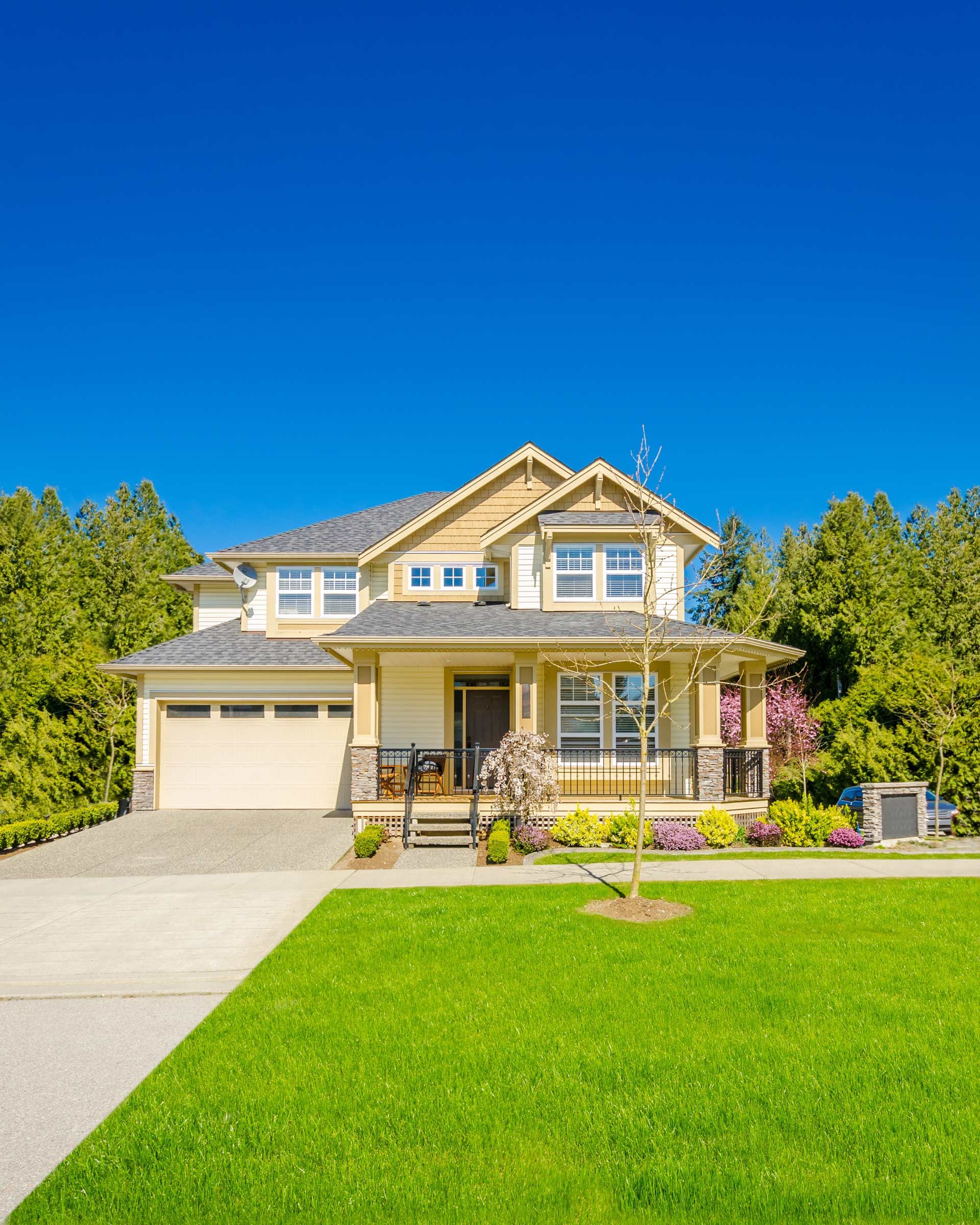 Two-story beige house with a green lawn, driveway, and blue sky.