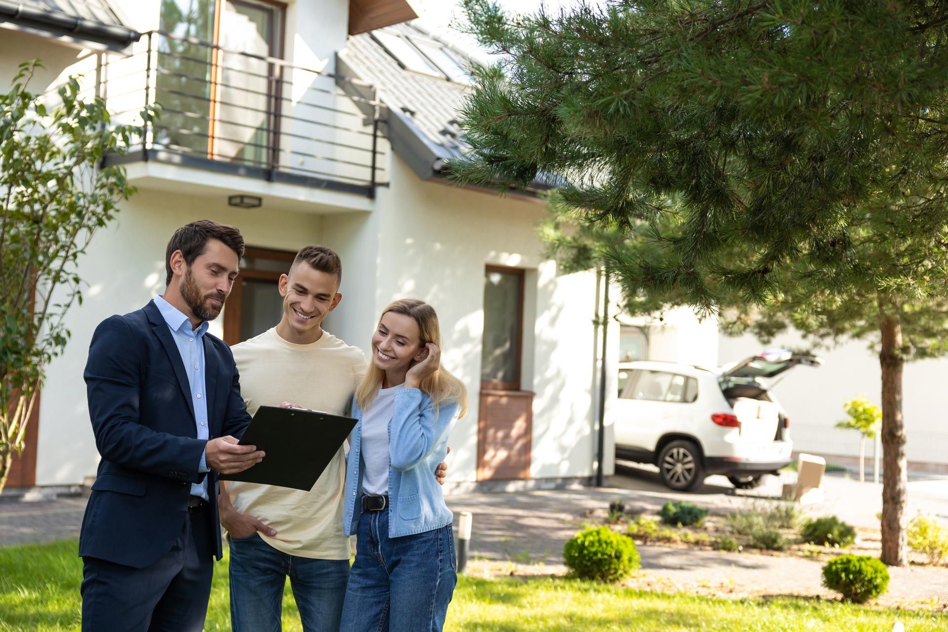 Real estate agent showing paperwork to a couple in front of a house.