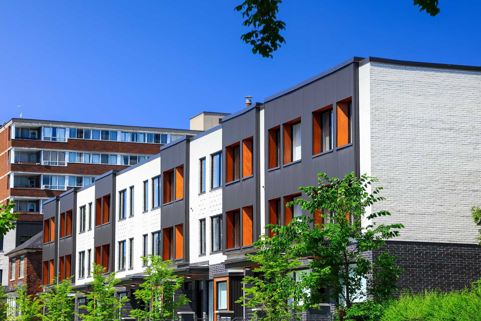 Row of modern townhouses with dark gray, white, and orange accents under a blue sky.