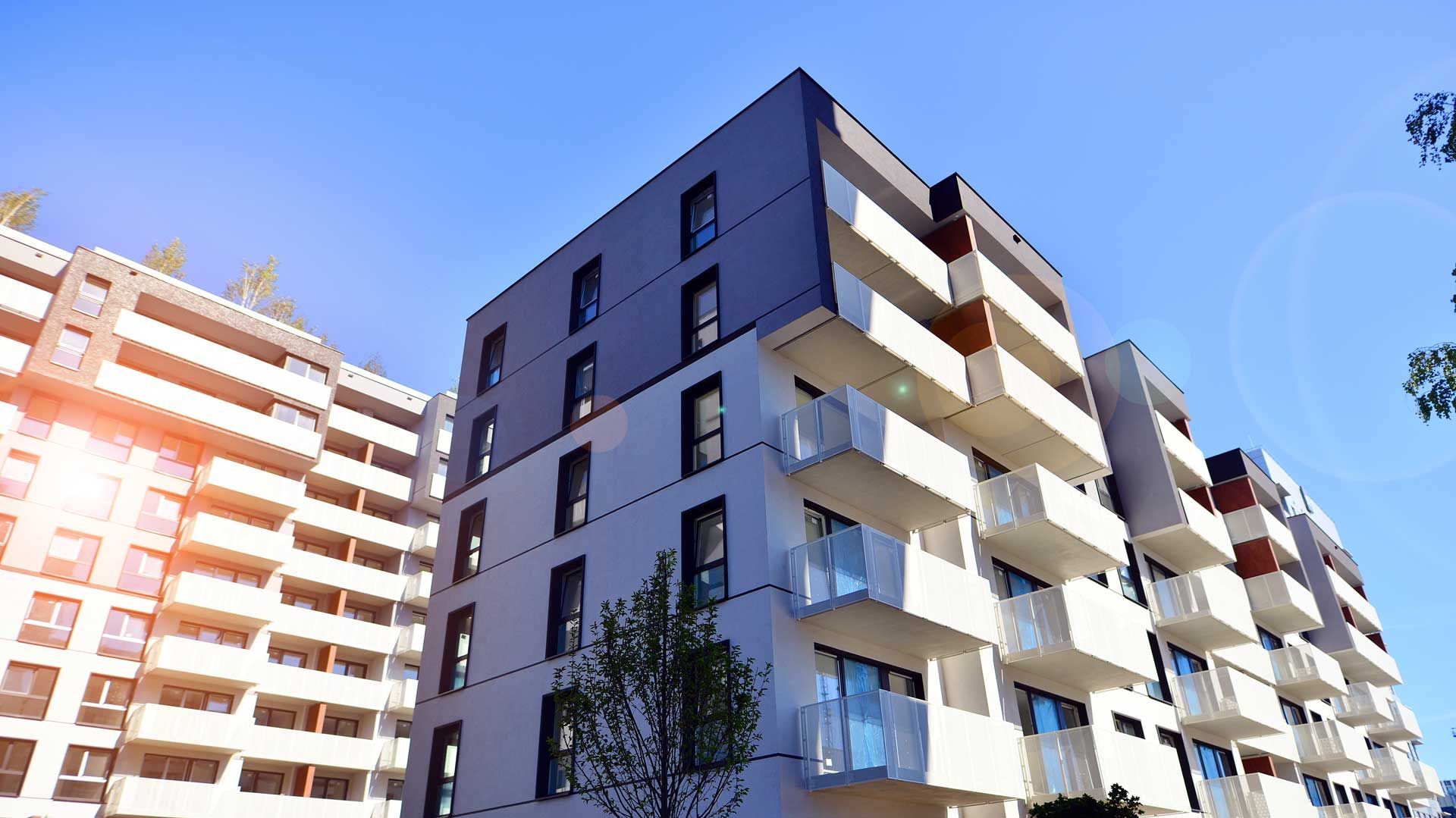 Modern apartment buildings with white balconies against a blue sky.