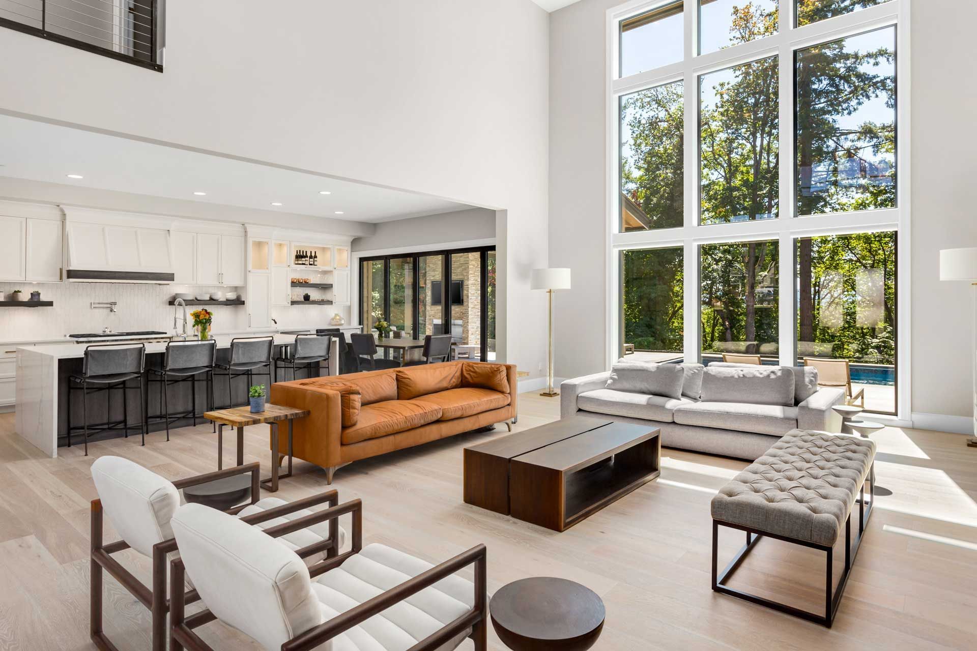 Spacious, modern living area with kitchen, large windows, couches, and light wood flooring.