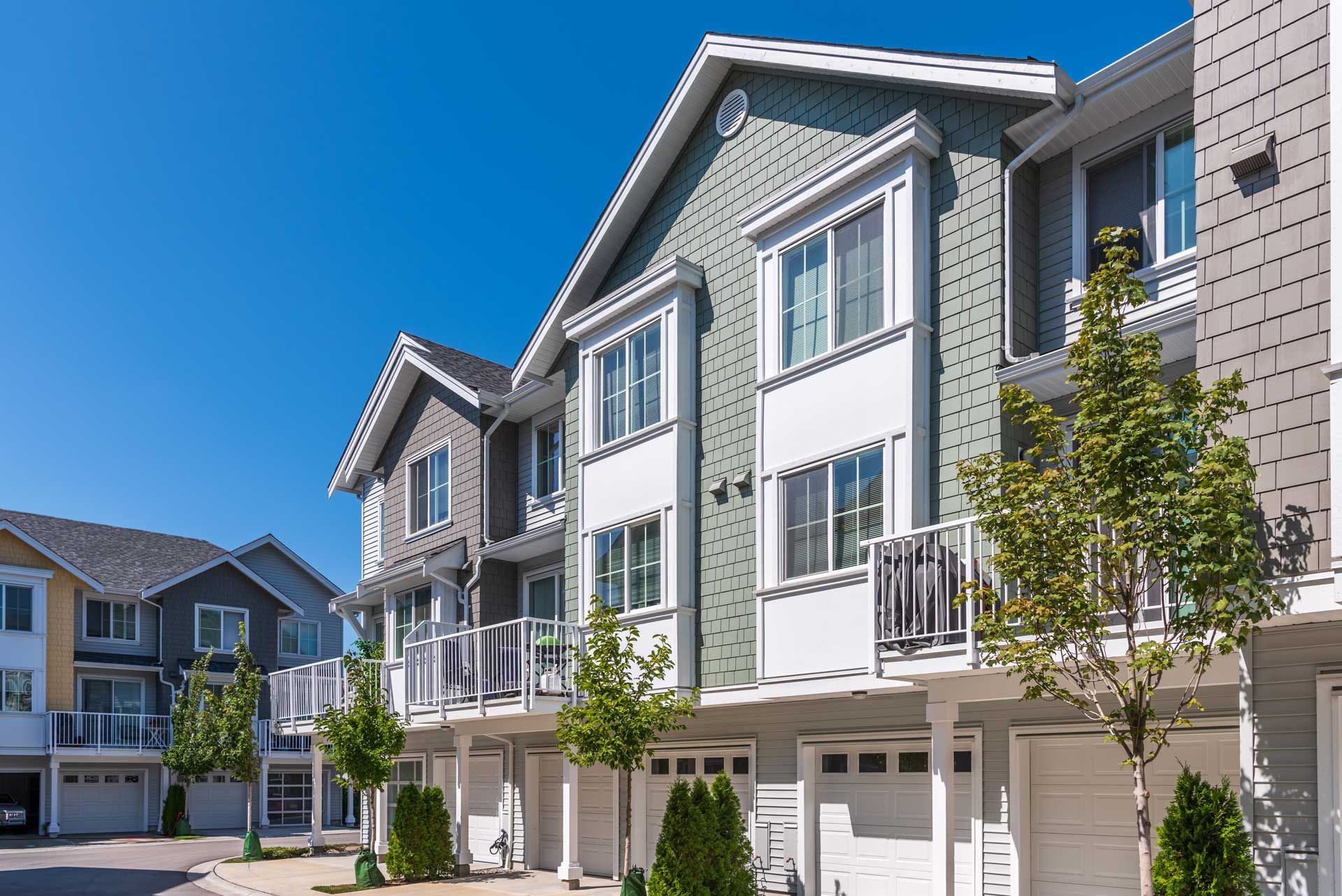 Townhomes with gray and green siding, white trim, and attached garages on a sunny day.