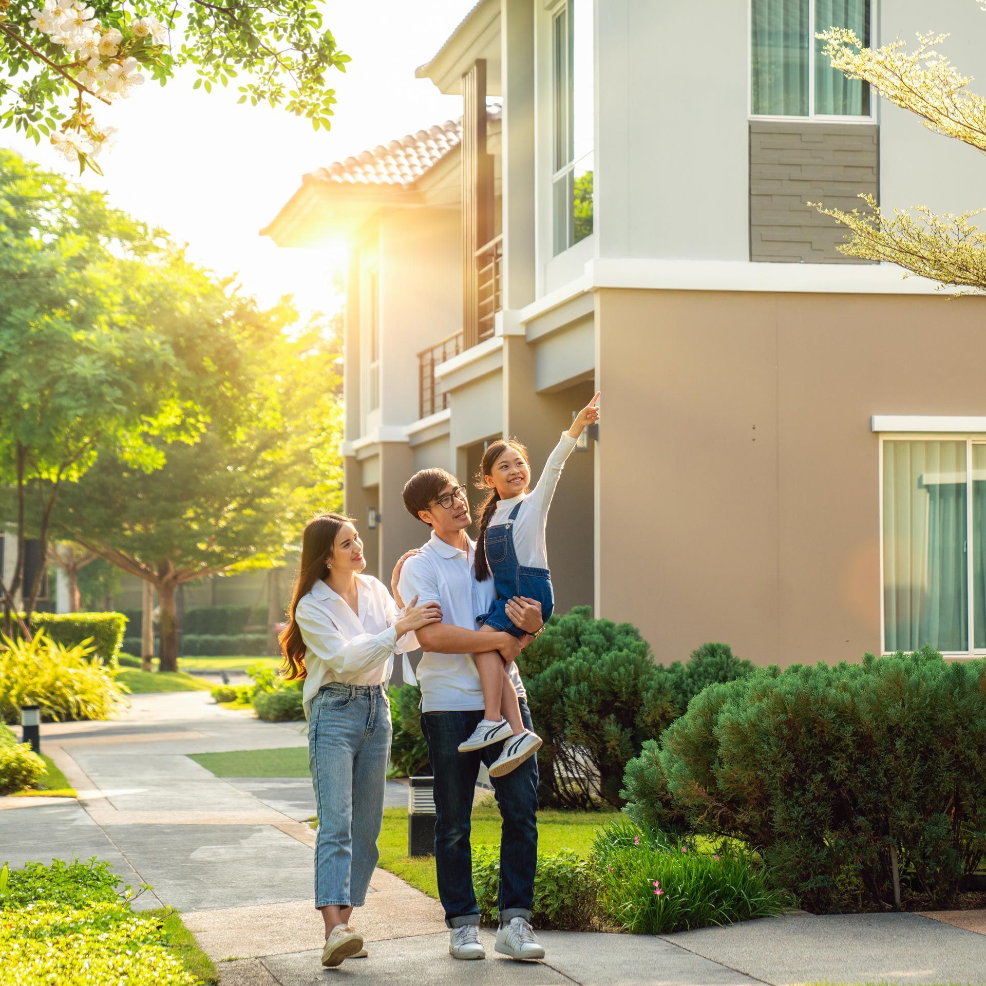 Family of three, holding key, standing outside a new house on a sunny day.