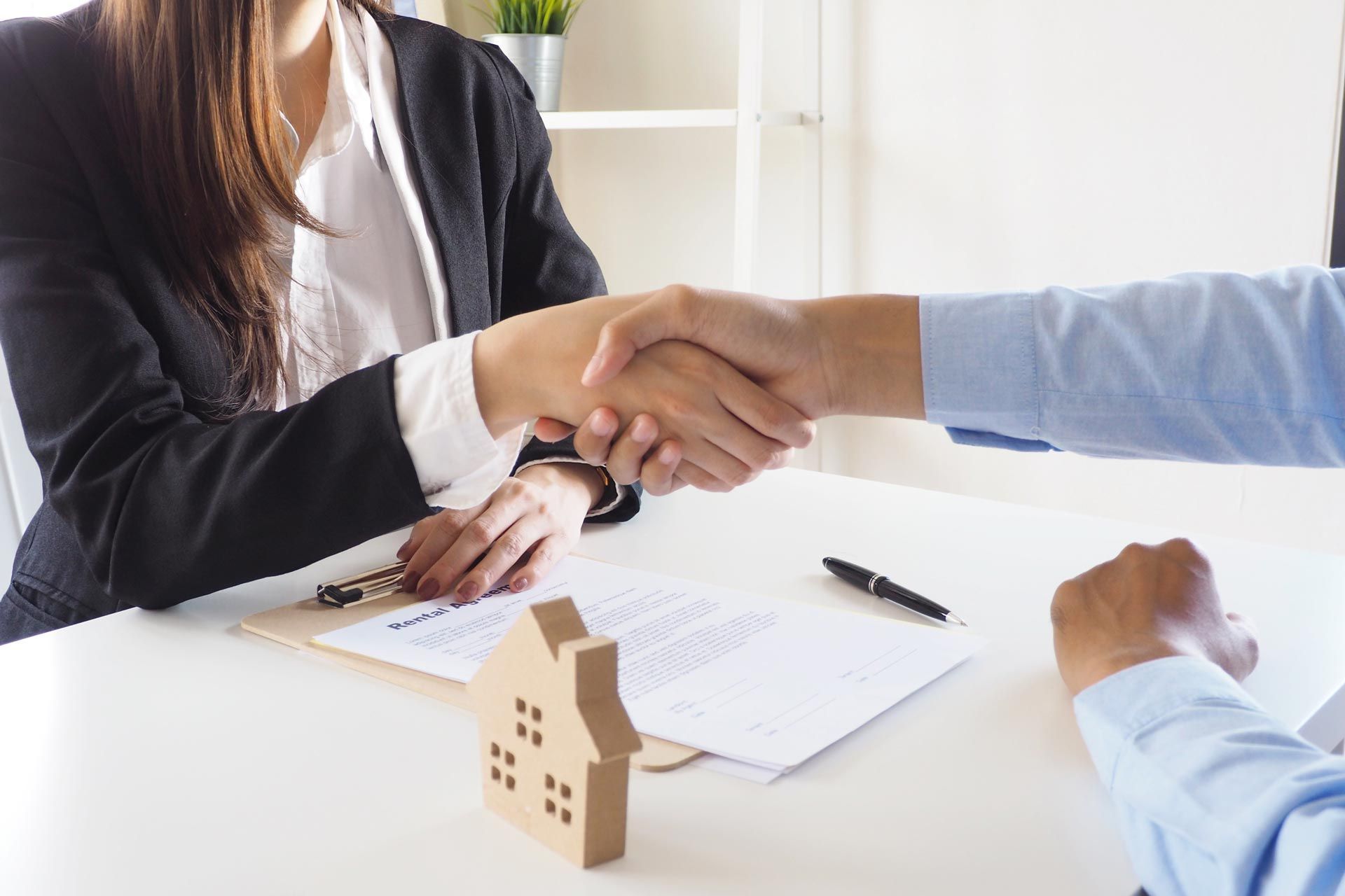 Person in a black blazer shakes hands with another person at a table, real estate documents present.