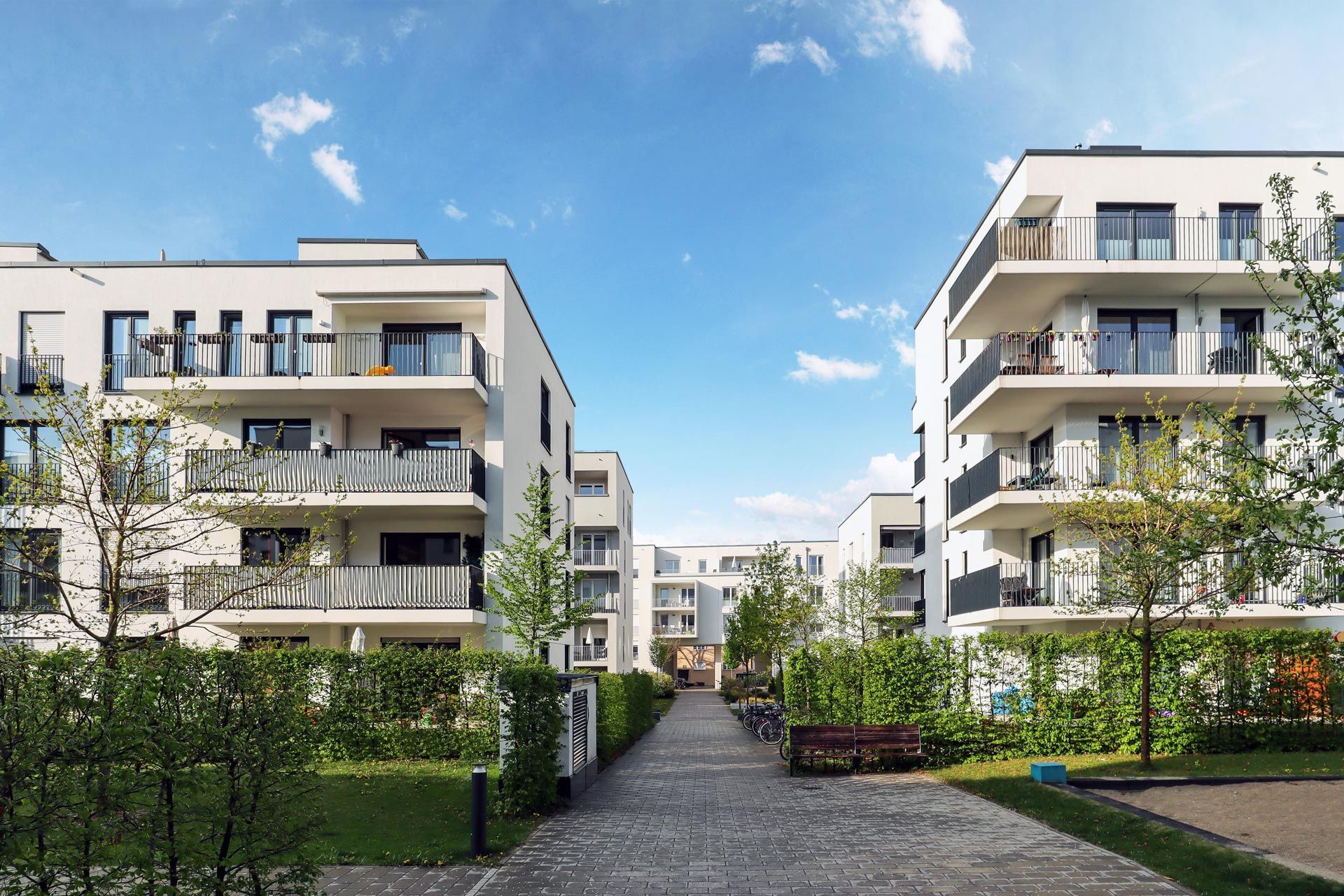 Modern white apartment buildings with balconies, pathway, and blue sky.