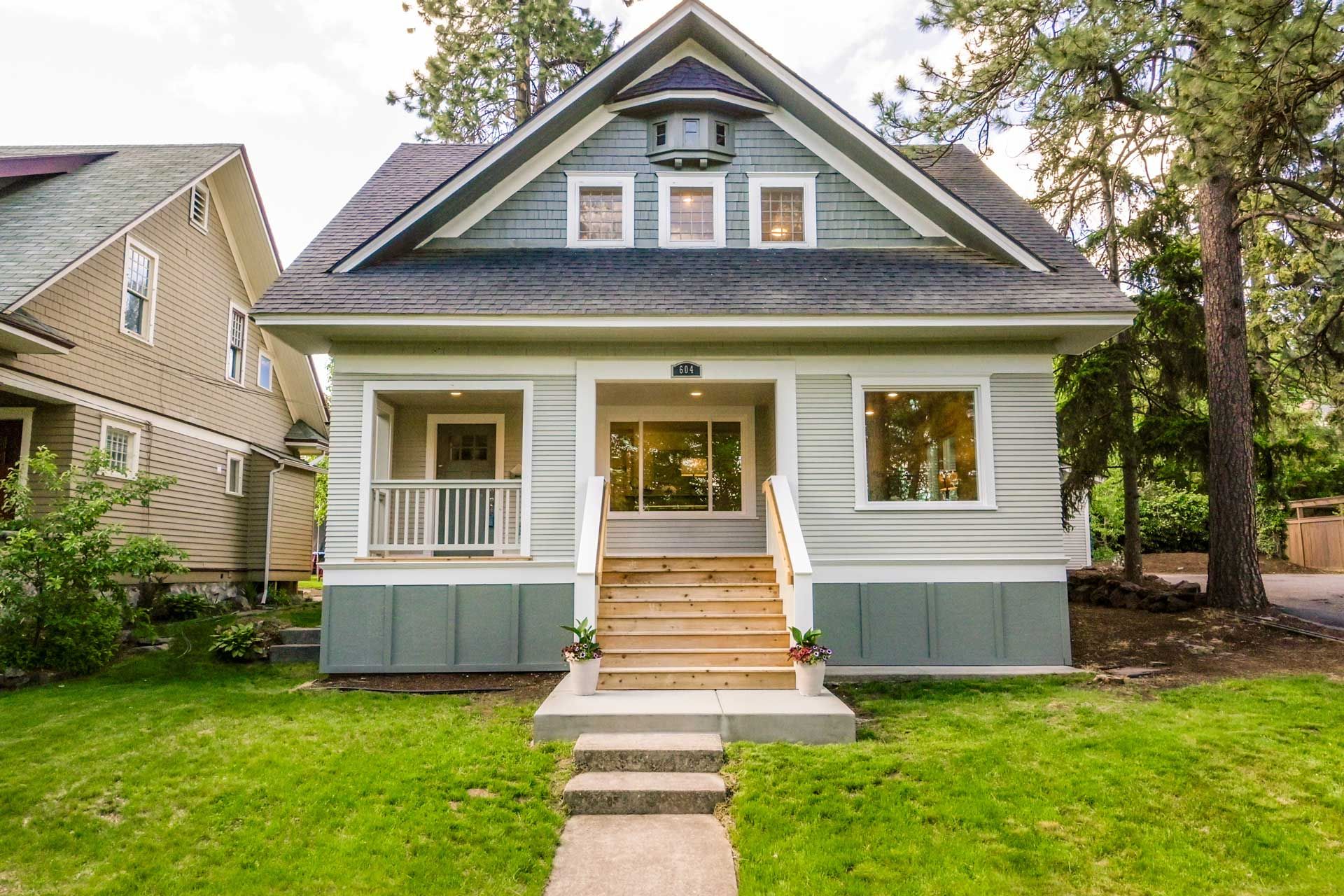A light green craftsman-style house with a front porch, steps, and a walkway.