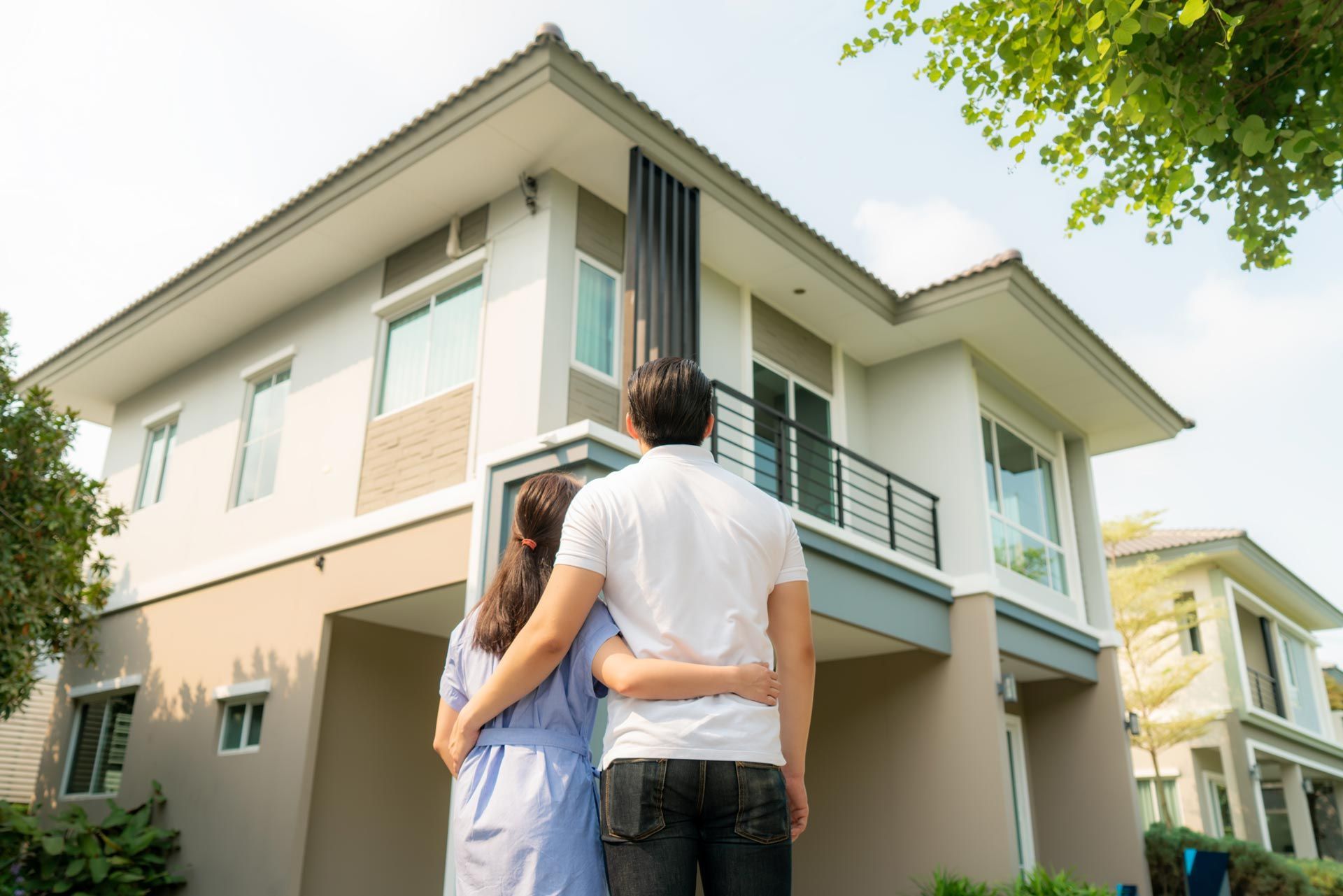 Couple looking up at a two-story modern house, sunny outdoor setting.