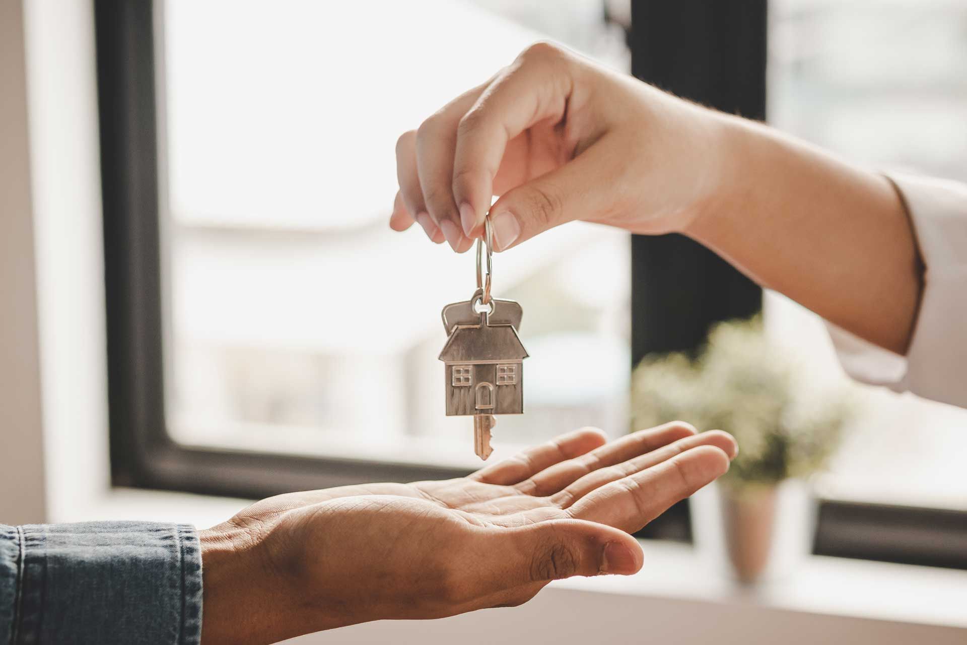 Hand passing house key to another hand.