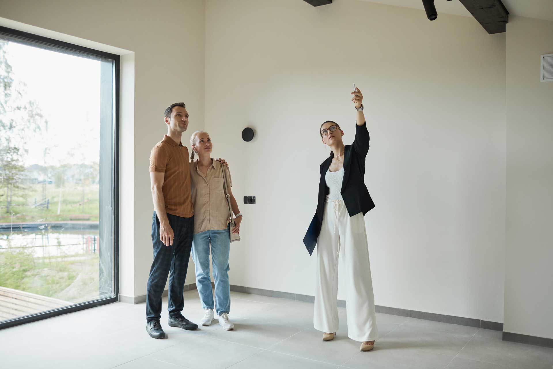 Real estate agent showing a couple a room in a modern house; agent pointing up.