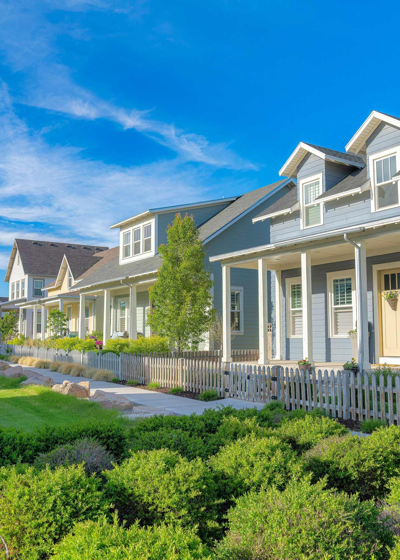 Row of pastel-colored houses with white porches and picket fence under a bright blue sky.