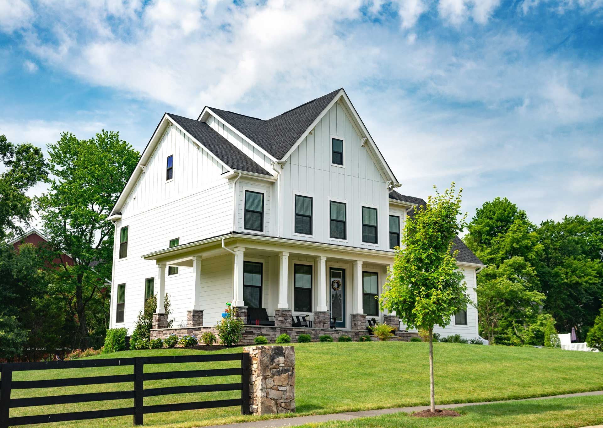 White farmhouse with black trim, green lawn, and blue sky.