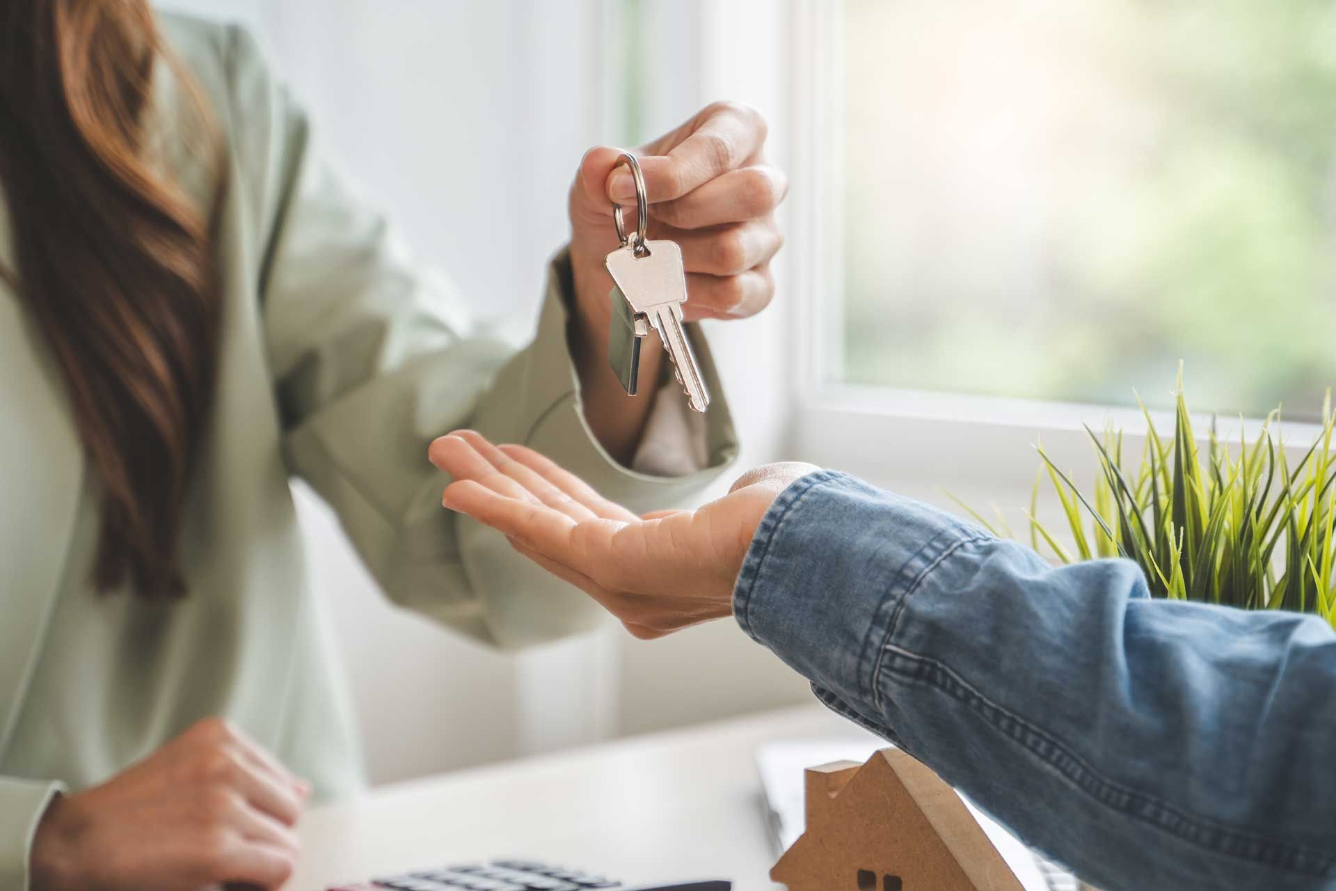 Person handing keys to another person near a small house model.